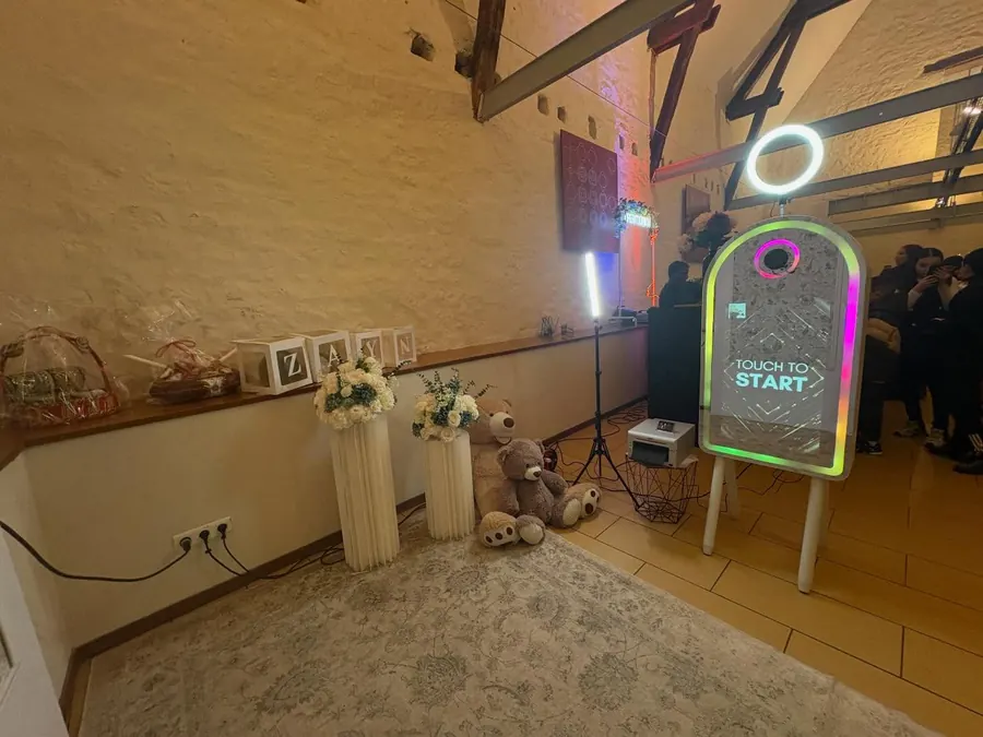 Photobooth miroir près d’un décor floral et de peluches pour une fête de naissance.