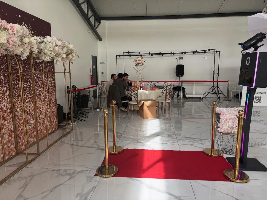 Photobooth classique installé dans une salle de réception décorée de fleurs, avec tapis rouge.