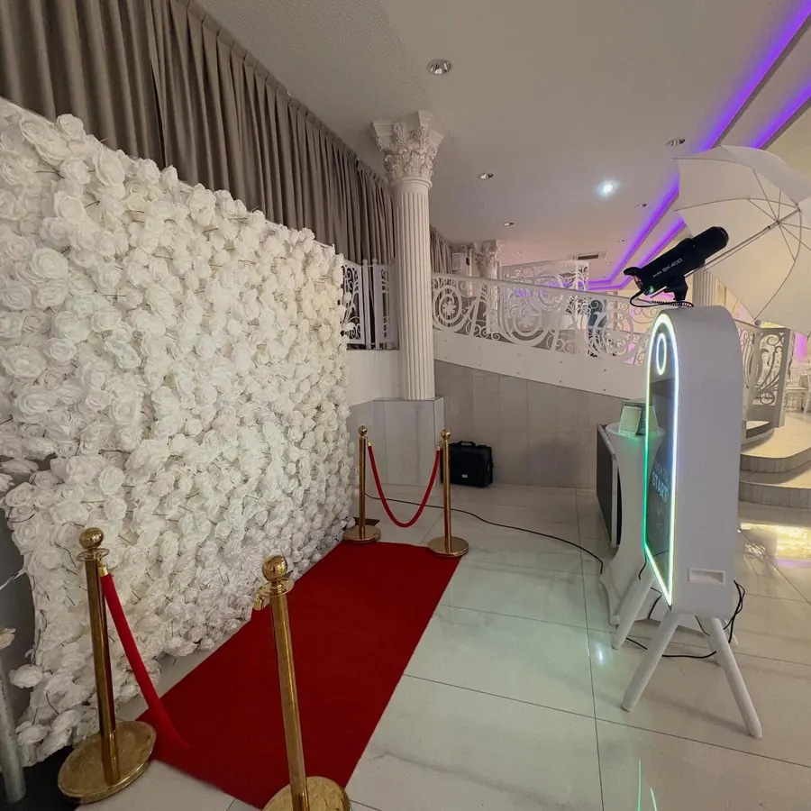 Photobooth miroir avec contour lumineux installé devant un mur de roses et un tapis rouge.
